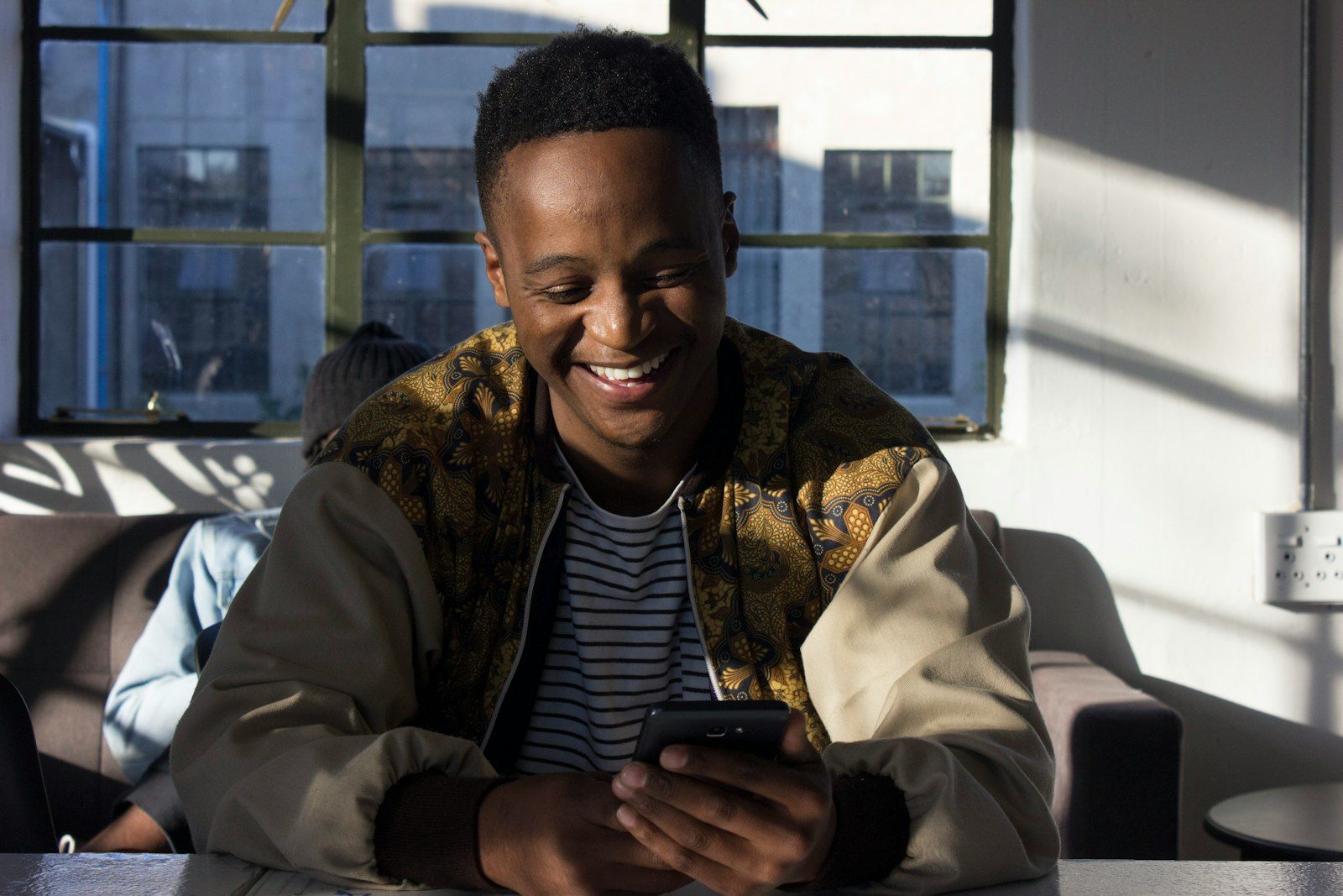 Man smiling while using a mental health app on his phone in a sunlit room