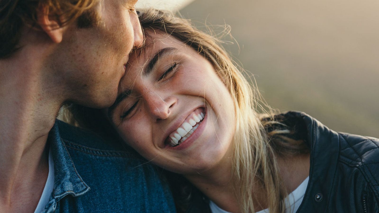 Young man kissing a smiling woman's forehead in warm evening light