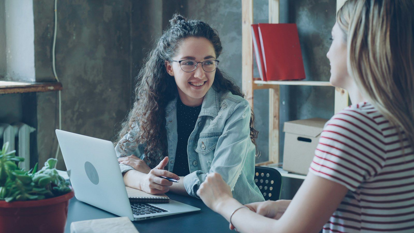 Counselor and client talking warmly at a desk with a notebook and laptop between them
