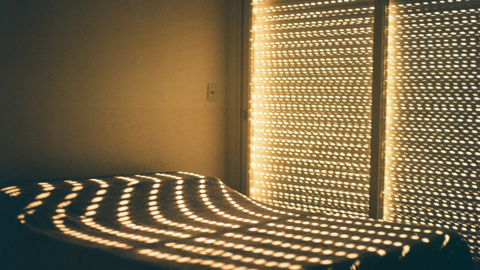 Warm morning sunlight filtering through blinds onto a bed in a quiet bedroom