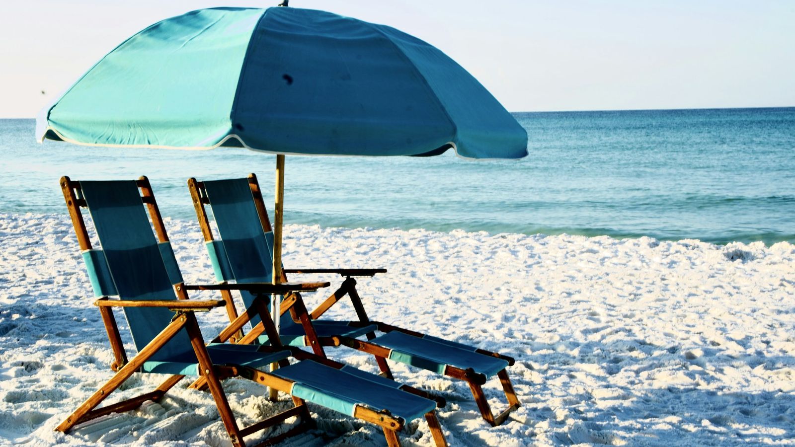two wooden beach chairs facing the ocean on a sunny day