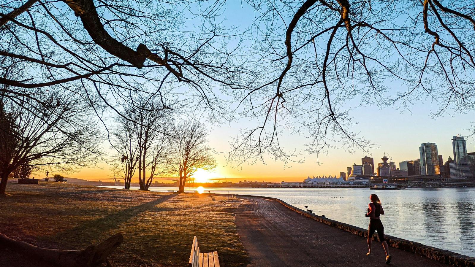 Person jogging along a waterfront path at sunrise