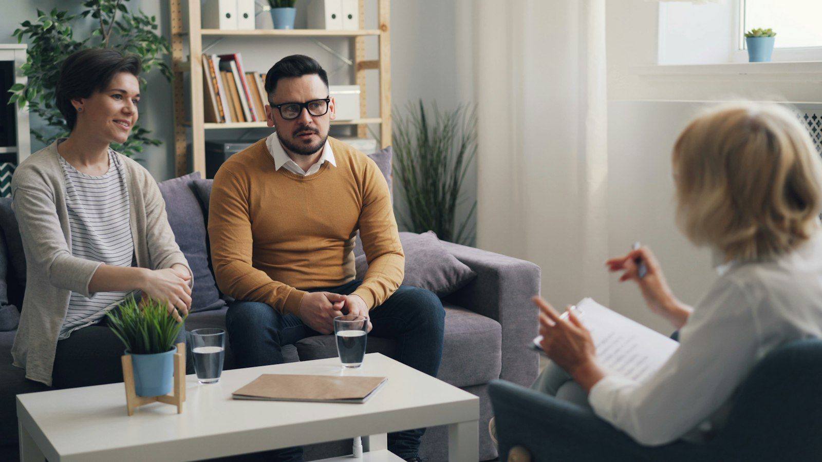 Couple sitting side by side on a couch, talking calmly with a counselor