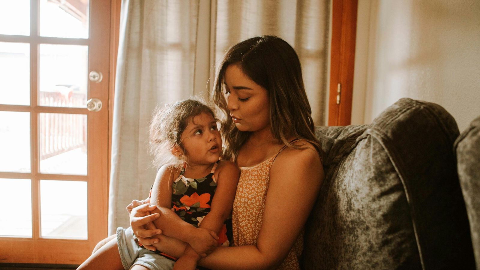 Mother holding her young daughter on a couch at home
