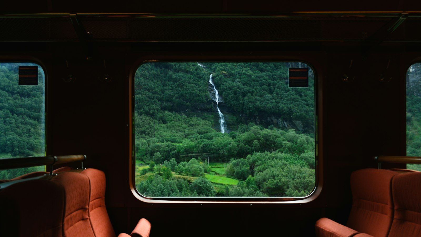 A green hillside and waterfall seen through the window of a train