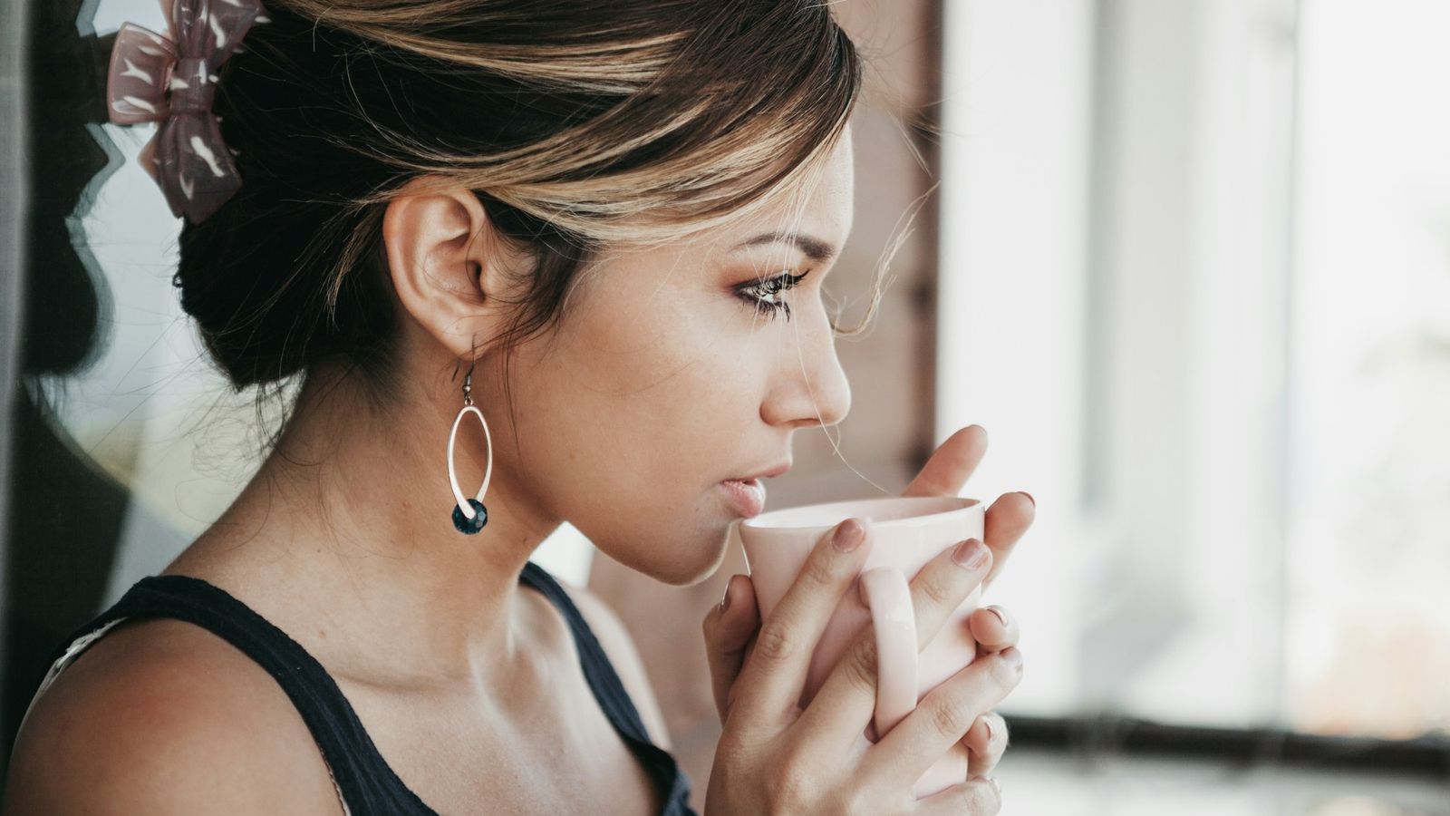 Woman holding a mug and looking thoughtfully out a bright window