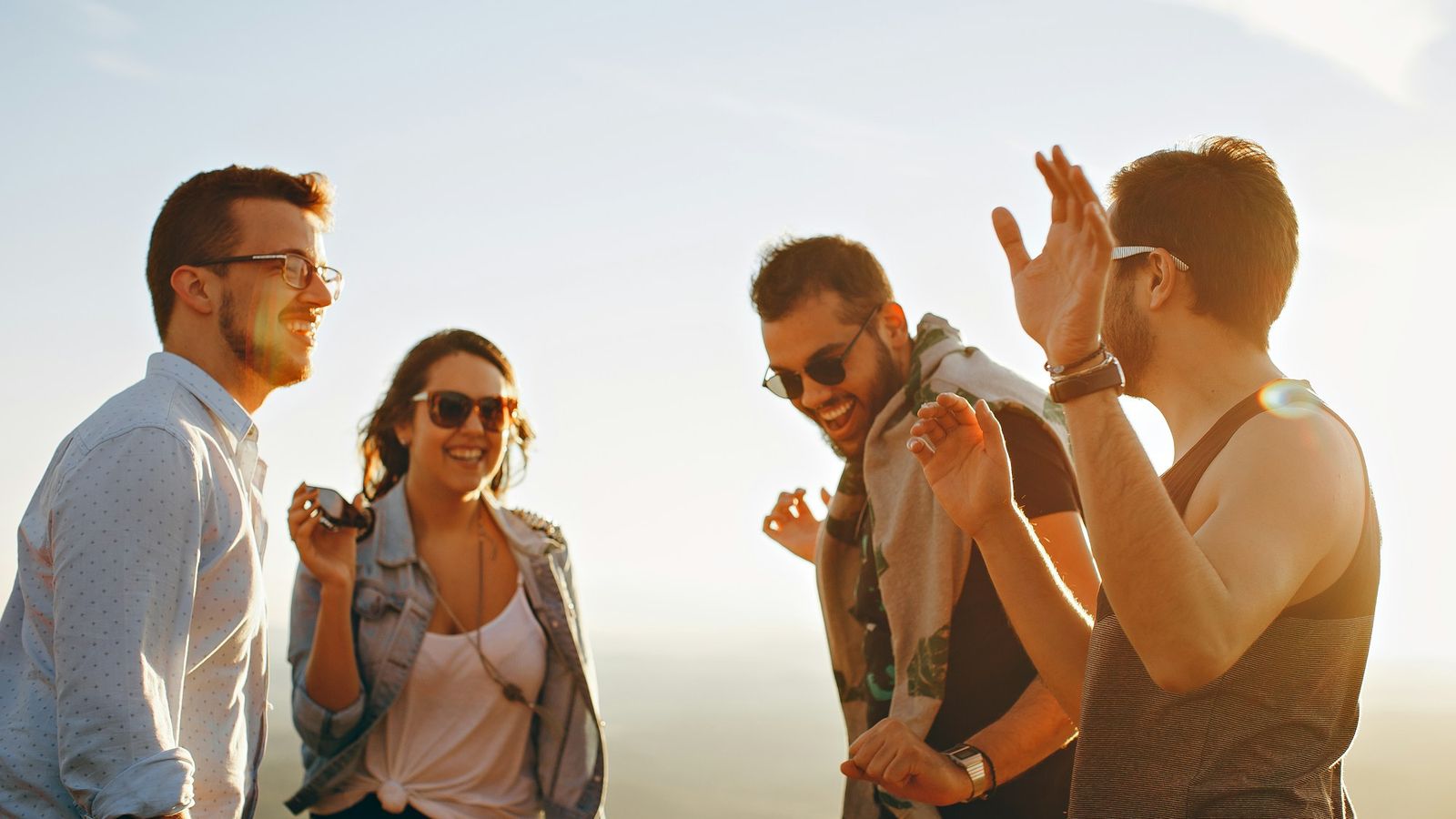 Four friends laughing together outdoors in warm golden hour light