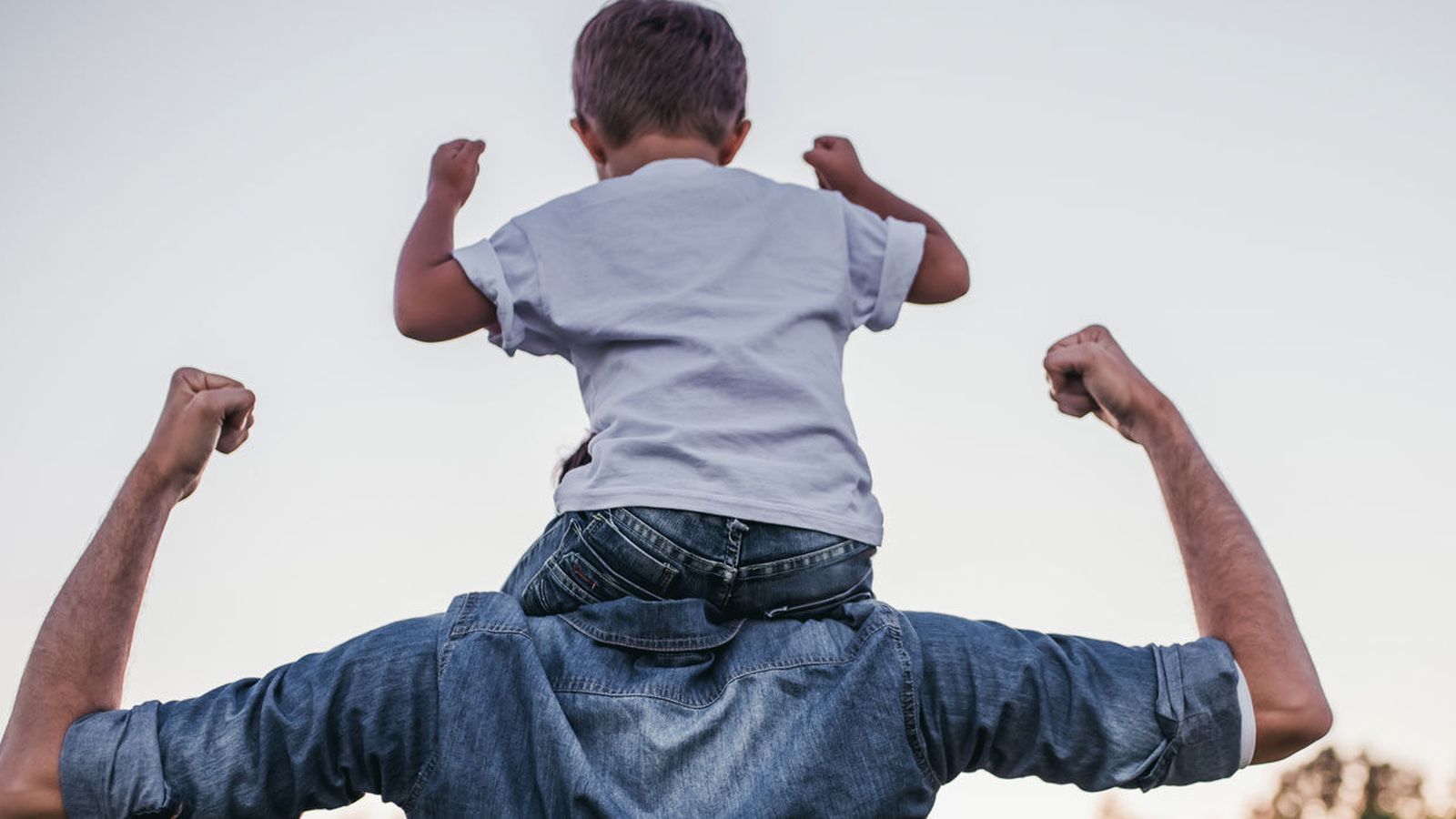 Child riding on a parent's shoulders, both flexing their arms in a strong pose