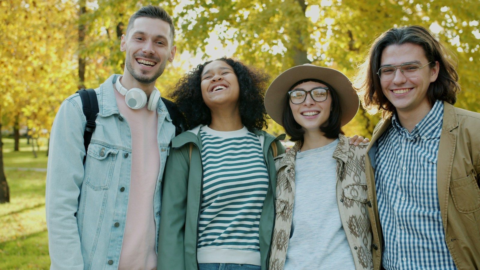 Four friends laughing together in a park on an autumn day