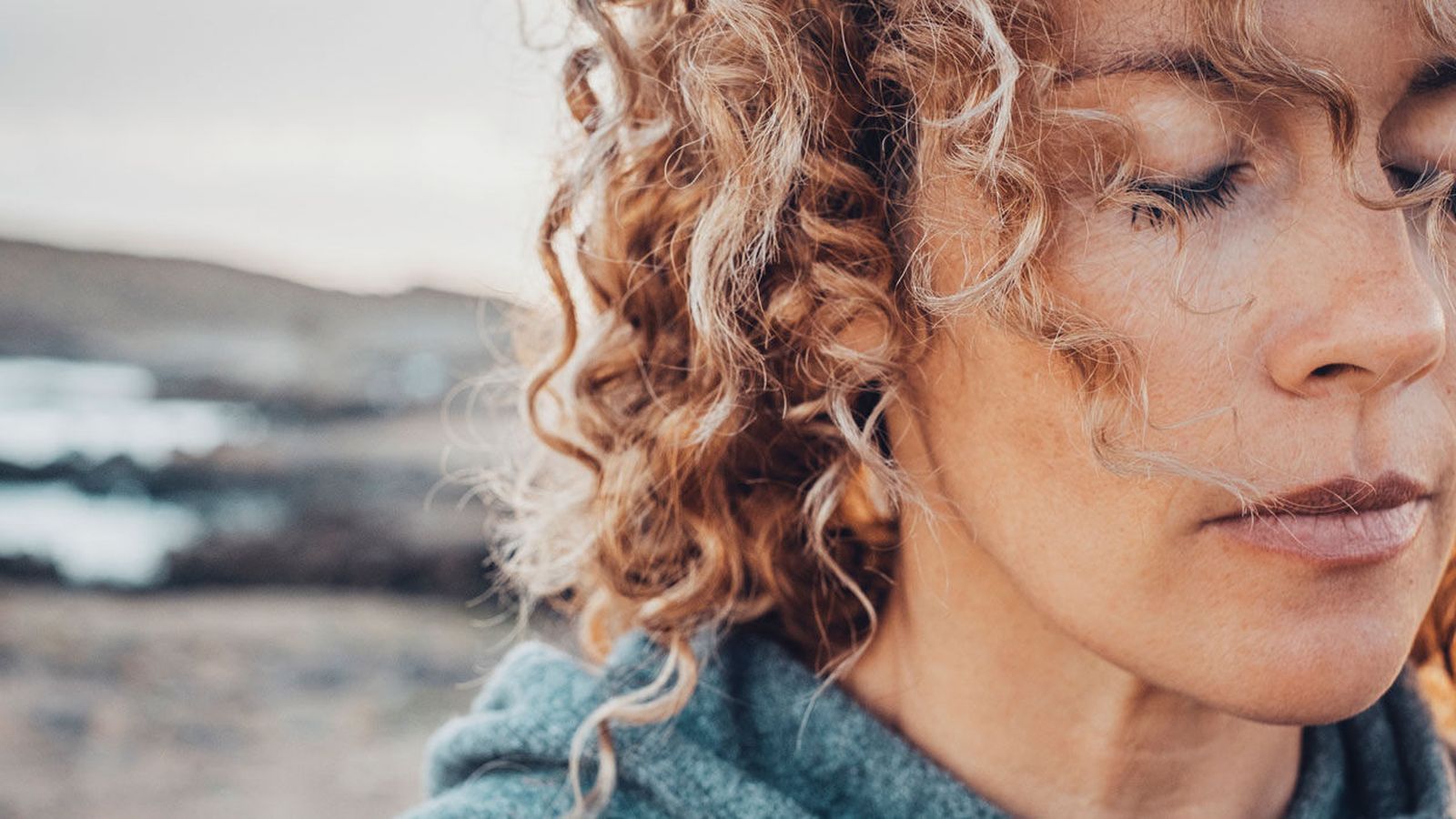 Close-up of a woman with curly hair pausing in quiet reflection by the sea