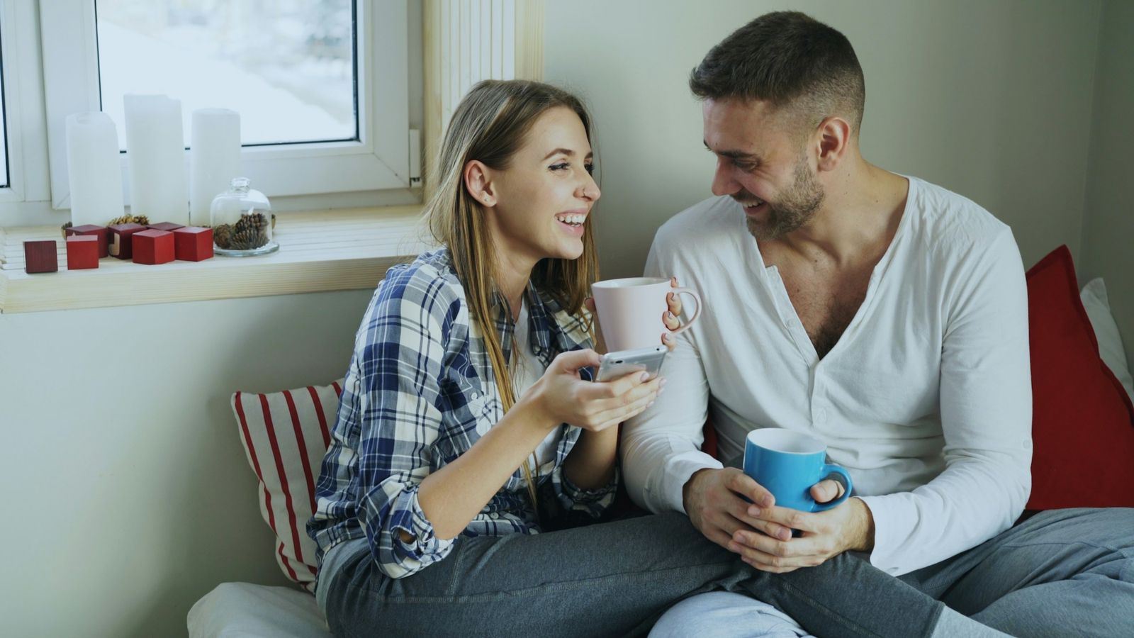 A young couple smiling and talking over coffee by a bright window
