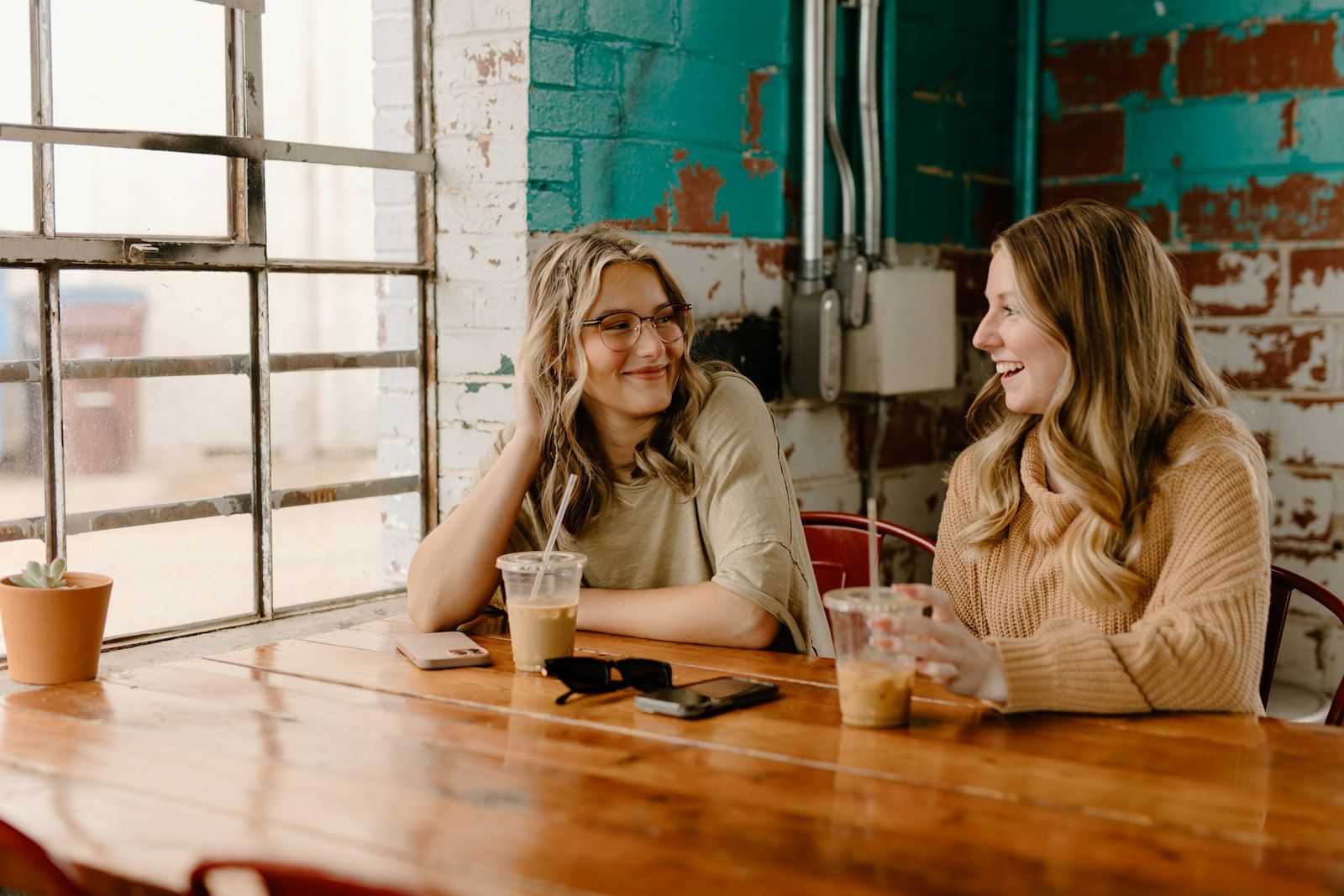 Two adult friends laughing together over coffee at a cafe table