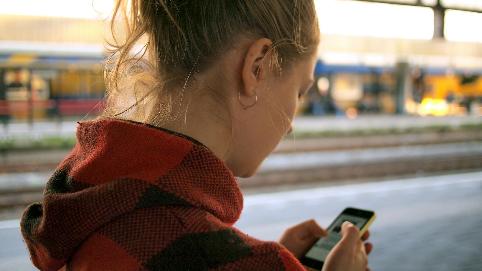 A young person in a plaid hoodie checking a smartphone, seen from behind