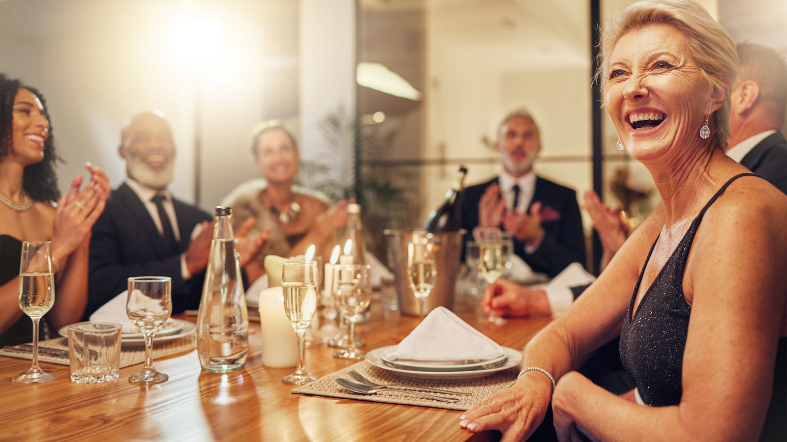 Friends laughing together around a candlelit dinner table, sharing a meal