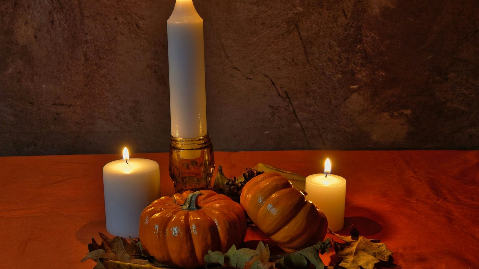 pumpkins and lit candles resting on autumn leaves