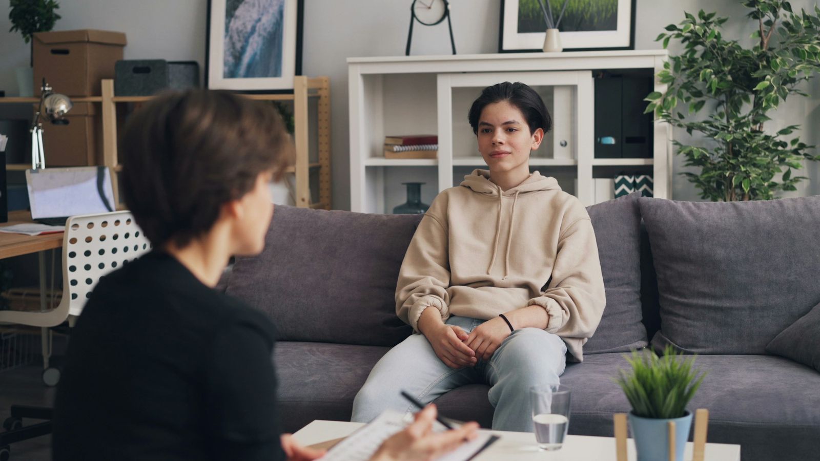 Therapist with a clipboard talking with a young man during an in-person counseling session