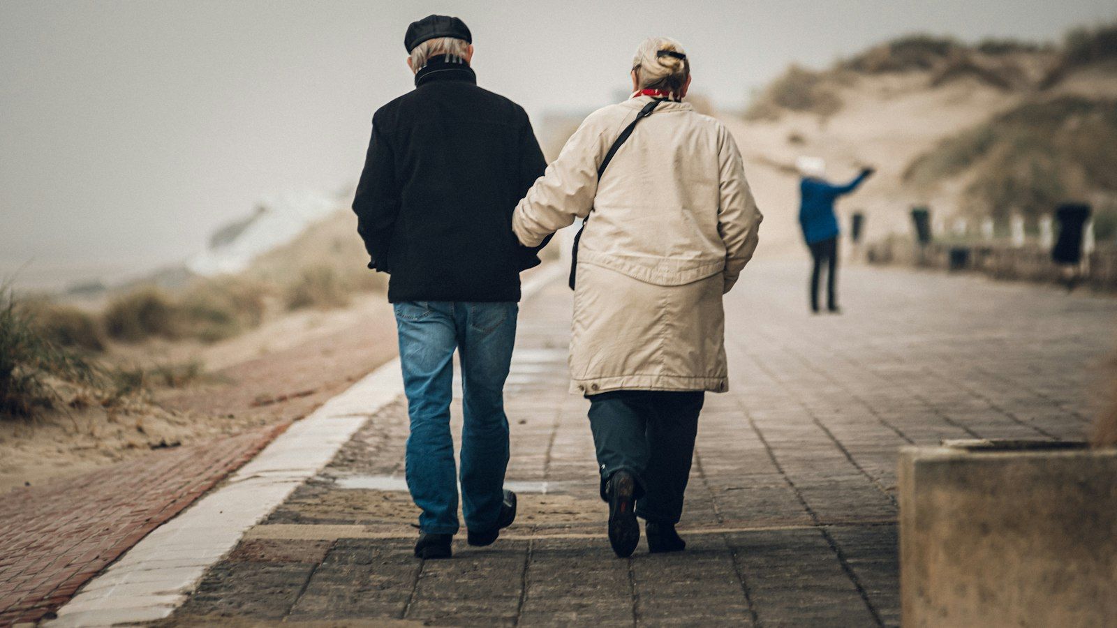 An older couple walking arm in arm along a seaside path, seen from behind
