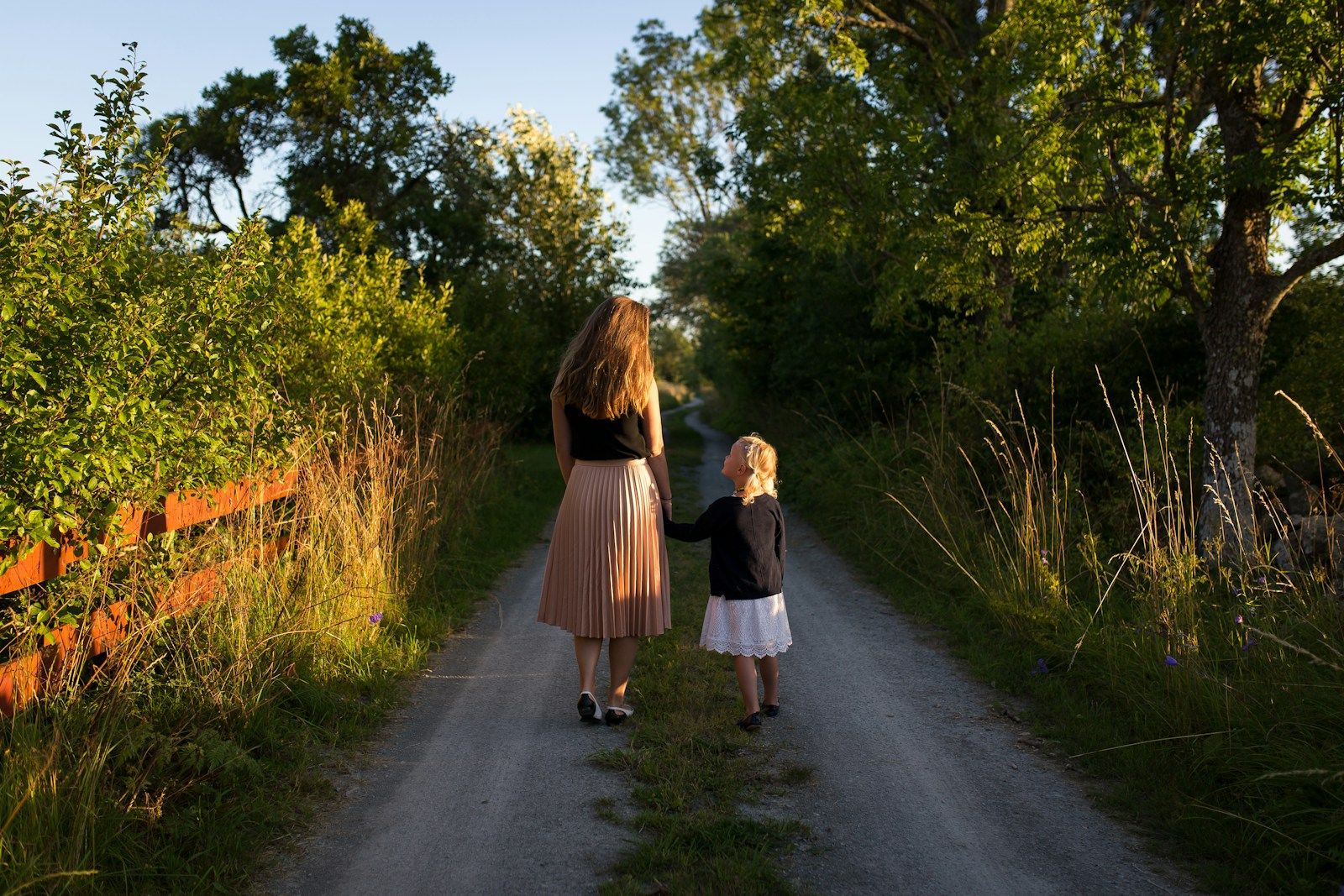 Mother and daughter walking together down a sunlit country road