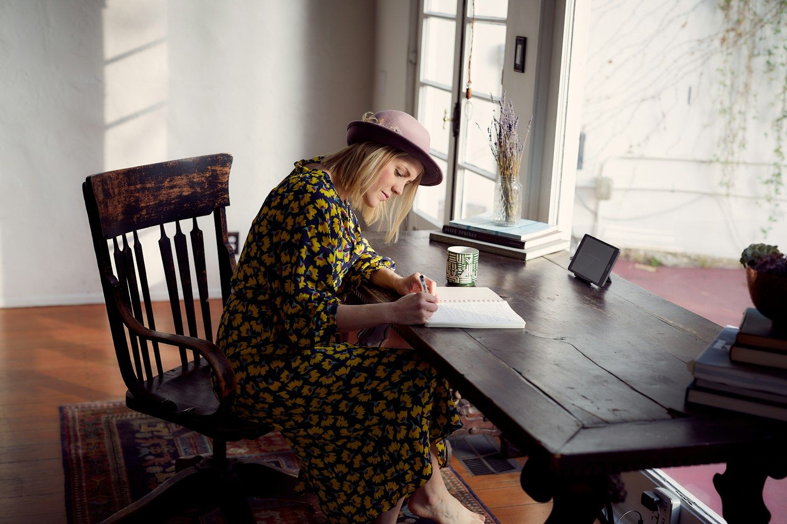 Adult sitting at a table by a sunny window, calmly writing notes in a notebook