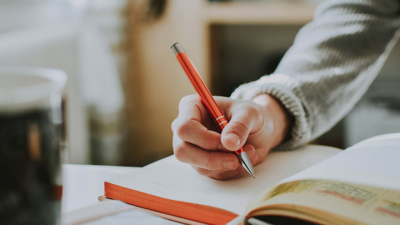 Close up of a hand writing in a journal with an orange pen